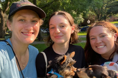 Chicago Urban Pets Staff with Owner, Stephanie, posing in a park.  They would two tiny puppies, who are booping noses.