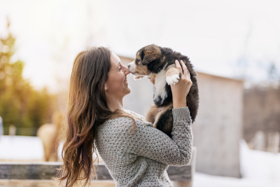 Woman in gray sweater holding a tricolor puppy outdoors.
