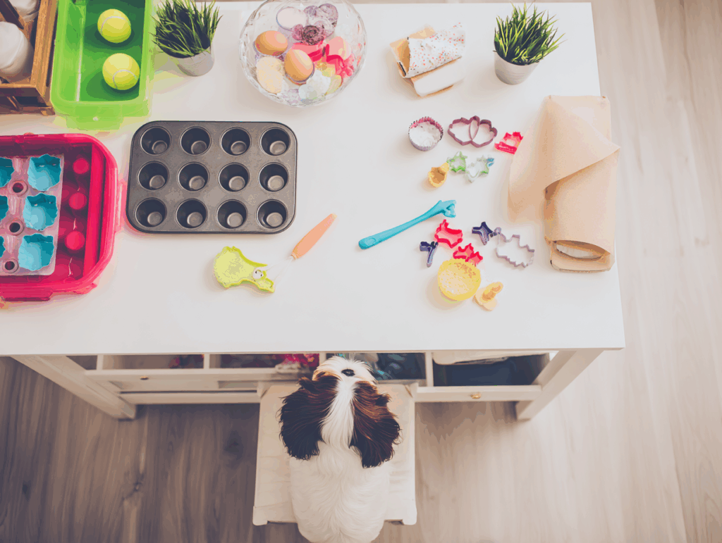 Table with baking items and tools, with a small dog looking up at it.